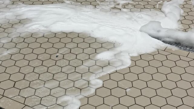 Foam and water being pushed across a tiled floor with a squeegee during an industrial washdown, highlighting sanitation workflow.