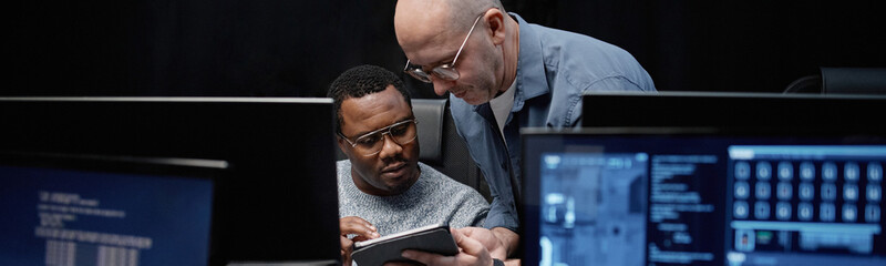 Header of young Black man and middle aged Caucasian man collaborating while using digital tablet in...