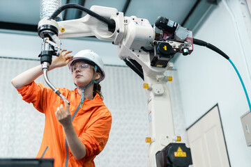Female engineer operating industrial robotic arm in smart factory environment, showcasing modern automation, advanced technology, and innovation in manufacturing processes.