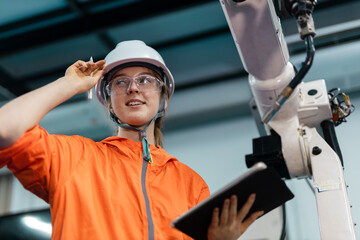 Female engineer using tablet to control robotic arm in smart factory, showcasing automation, industry 4.0, advanced manufacturing technology for efficient production management.