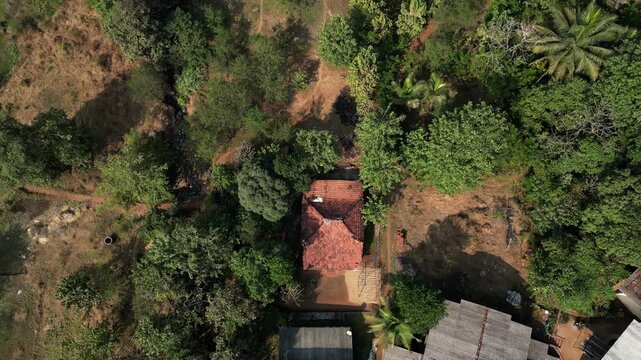 Downward aerial shot of a village house, revealing the rooftop from top to bottom. Traditional rural architecture, natural surroundings, calm atmosphere, and authentic countryside lifestyle.