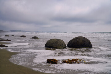 Moeraki Boulders overcast beach scene, rough sea, foamy shoreline, New Zealand, sunset