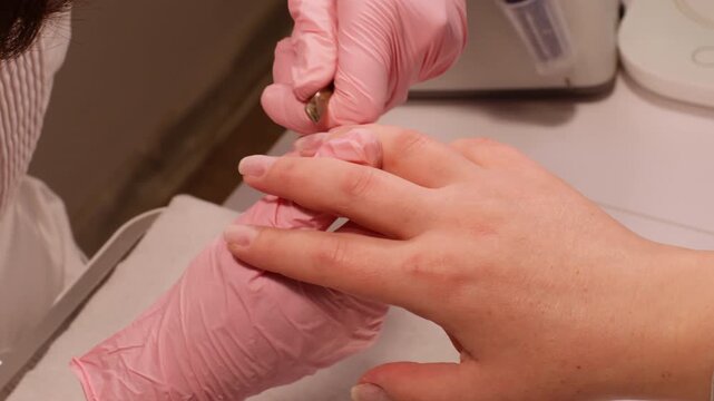 Modern fingernails process. Salon procedure. Beautician female master hands in protective gloves cutting cuticle nail skin on clients finger using forceps for beauty.