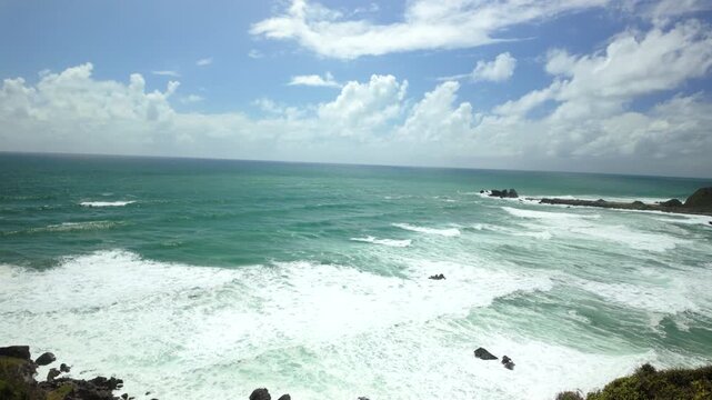 Turquoise ocean panorama with rolling surf and distant rocks