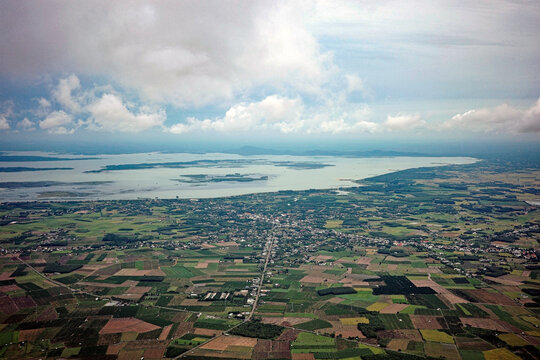 aerial view of dau tieng lake and patchwork agricultural fields seen from Ba Den mountain summit in Tay Ninh, vietnam. vast rural landscape scenery under cloudy sky.