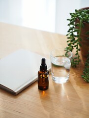 Essential oil bottle with glass of water and notebook on wooden desk