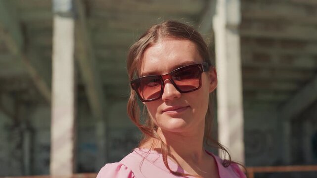 gritty underpass portrait caucasian woman sunglasses. urban explorer posing beneath concrete bridge, graffiti backdrop, warm sunlight catching cheek, confident gaze, street fashion attitude,