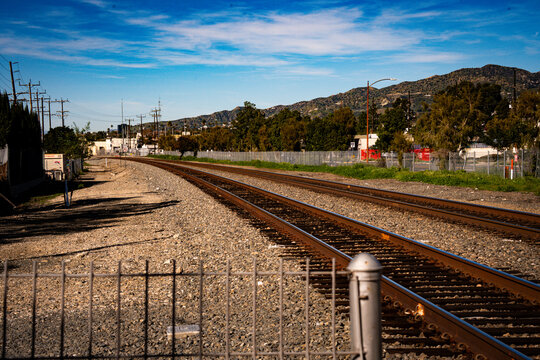 Double railroad tracks curve through a landscape with distant mountains and blue sky