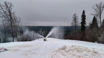 A snow cannon sprays fine powdery snow across a landscape.