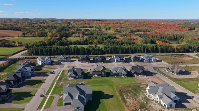 Aerial drone view of a new suburban housing development under construction in Alton, Caledon, Ontario, Canada, with fall forest colors and rural countryside in the background.