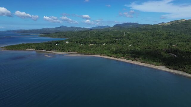 Aerial drone footage of a remote sandy beach on Tablas Island near Odiongan, Philippines, featuring dense green palm forest and rolling mountains in the background on a bright sunny day.