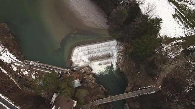 Drone lifts up from Lechfall's icy dam in Fussen during winter, exposing snow-dusted spillway, churning rapids and forested rocky gorge. Crisp Bavarian hydro power.