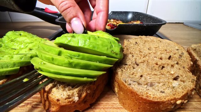 Close up of hand placing sliced avocado on whole grain bread in home kitchen