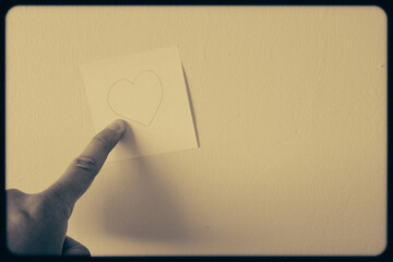 Vintage film style of finger pointing to sticky note with hand drawn heart on wall.
