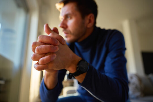 Portrait of worried man leaning on window and looking down with clenched fist at home. Concept of stress, anxiety, mental health problems, emotional tension and difficult life situation