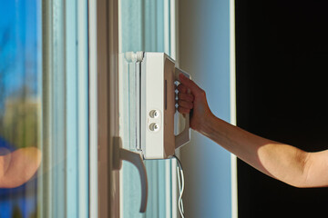 Woman starting robotic window cleaner on glass surface of window. Using automatic device for window cleaning at home. Smart home appliance concept