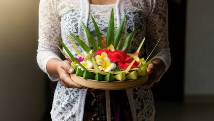 Balinese woman holding a traditional offering with flowers and leaves.