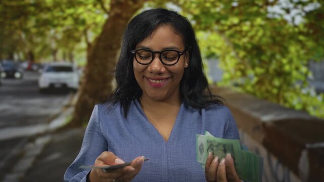Woman holding and counting green ringgit bills with both hands on city street under trees; prosperity.