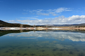 Sunny winter morning cloudscape over Grass Valley Reservoir in Harvey Gap State Park, Colorado reflected in reservoir's calm water.