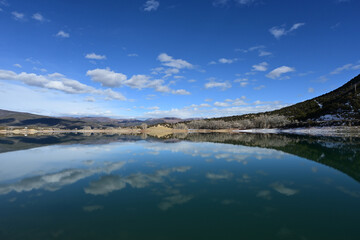 Sunny winter morning cloudscape over Grass Valley Reservoir in Harvey Gap State Park, Colorado reflected in reservoir's calm water.