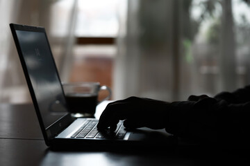 Silhouette of Hands Typing on Laptop in Low Light, With a Coffee Cup in the Background