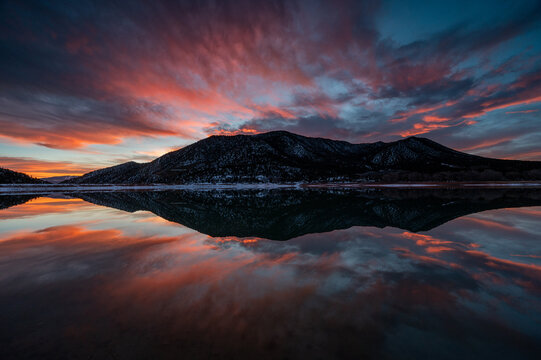 Intensely colorful sunset cloudscape over Grass Valley Reservoir in Harvey Gap State Park, Colorado reflected in reservoir's calm water.