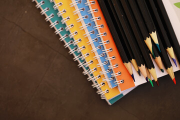 Obraz premium Colorful Spiral Notebooks and Pencils on Brown Surface Create Vibrant Workspace Aesthetic