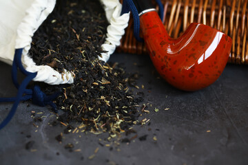Obraz premium Aromatic Pipe Tobacco Spilled from Pouch with Classic Smoking Pipe on Dark Background