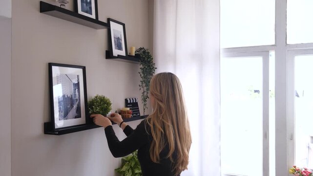 Woman arranging and organizing objects on a black shelf. Girl decorating a wall in a modern house interior. Cozy lifestyle scene with natural light. interior design and everyday domestic activity.
