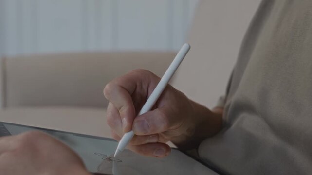 Close up shot from a clear side angle shows a male hand drawing on a graphic tablet with a stylus. The camera emphasizes smooth motion and focused digital drawing process. High quality 4k footage