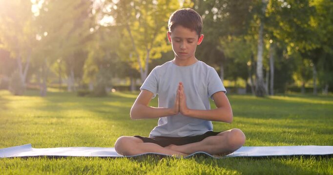 Child sitting calmly outdoors in park at sunset. Focused child practices emotional balance and self control in nature. Calm child develops concentration, confidence and healthy emotional skills.
