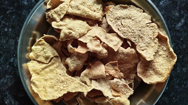 Crispy fried Papadum served in a steel plate on a dark marble surface