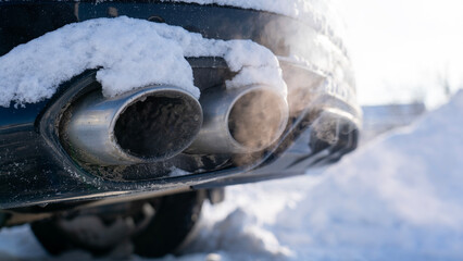 A car with its exhaust pipe smoking in the snow. The car is parked in the snow, and the smoke coming out of the exhaust pipe is visible