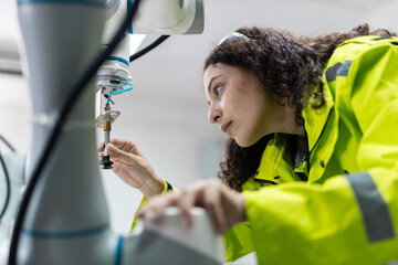 Female engineer closely inspecting and adjusting robotic arm components in high-tech industrial environment, symbolizing precision, innovation, smart automation.