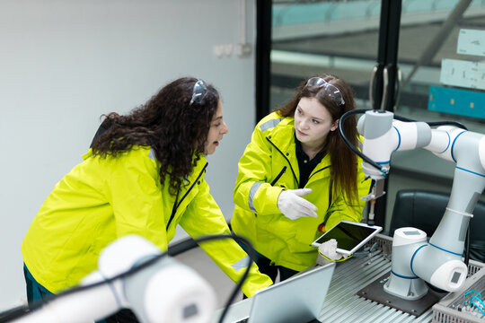 Female engineer using digital tablet to control or monitor robotic arm in modern industrial facility, representing smart manufacturing and automation technology. - Powered by Adobe