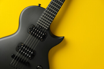 Fototapeta premium Stylish black electric guitar on a vibrant yellow background, top view.
