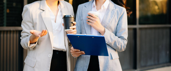 Two business women using tablet and coffee outside modern office, teamwork, communication, digital business, professional lifestyle