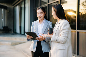 Two business women using tablet and coffee outside modern office, teamwork, communication, digital business, professional lifestyle