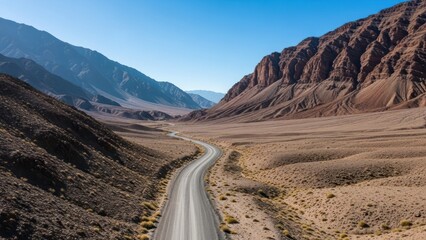 Fototapeta premium Winding asphalt road through arid landscape of majestic mountains and clear sky offering sense of