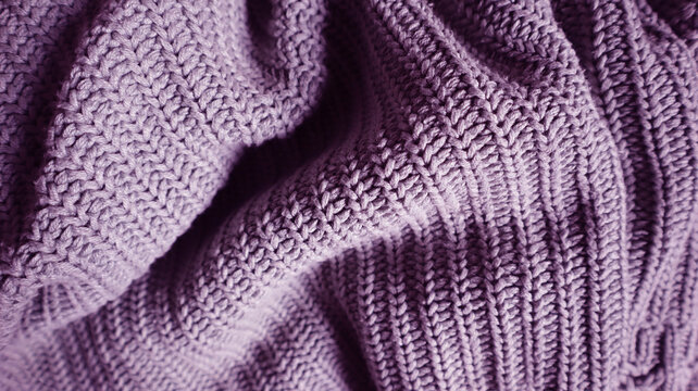 Close up of a knitted blanket or sweater texture in a beige, purple color. Cozy, warm background for autumn, winter or holiday concepts. Hand knitted, crumped stitch pattern. Warm clothiers.