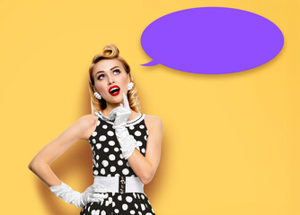 Surprised woman in pin up dress. Funny pinup emotional thinking cute girl, isolated yellow background. Purple empty mockup speech sign bubble. Sale ad concept image. Free text space