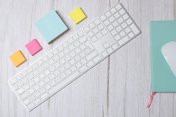 Horizontal top view of modern workspace with white keyboard, green notebook, mouse and colorful sticky notes on light wooden desk with copy space. Concept of creative workspace and productivity