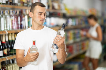 Young male shopper in casual clothes chooses vodka in grocery store
