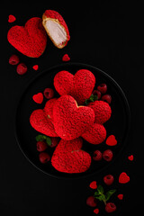 Heart-shaped profiteroles with red craquelin and raspberry cream &ndash; Valentine&rsquo;s Day dessert on a plate on a black background. Top view, copy space.