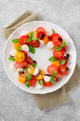 Caprese salad with cherry tomatoes, mini mozzarella and fresh basil with balsamic vinegar in a white plate. Healthy vegetarian meal.