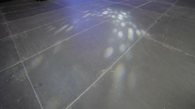 Bright rotating reflections scatter on cold floor creating light pattern. Glow results from overhead rig testing before concert setup begins