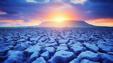 A dramatic sunset illuminates a vast landscape of jagged, fractured stone and rocky terrain beneath a colorful sky