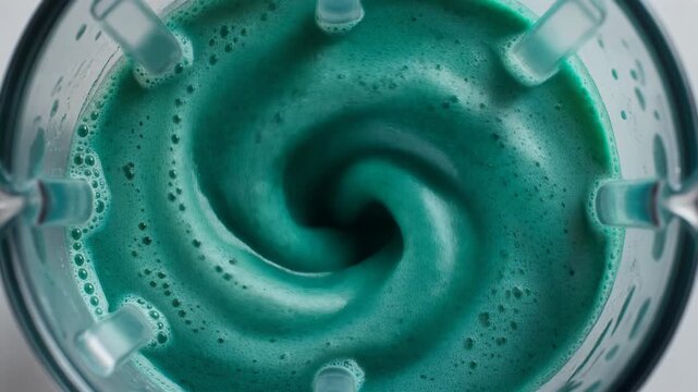 Vibrant blue-green healthy smoothie spirulina drink blending in high-speed blender jar creating a vortex whirlpool macro top-down view