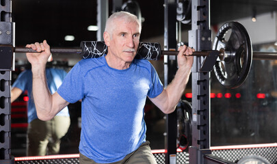 Elderly man in sportswear training with barbell in gym