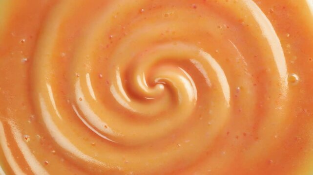 Abstract background of orange creamy texture swirling in a spiral pattern close-up of thick liquid or sauce